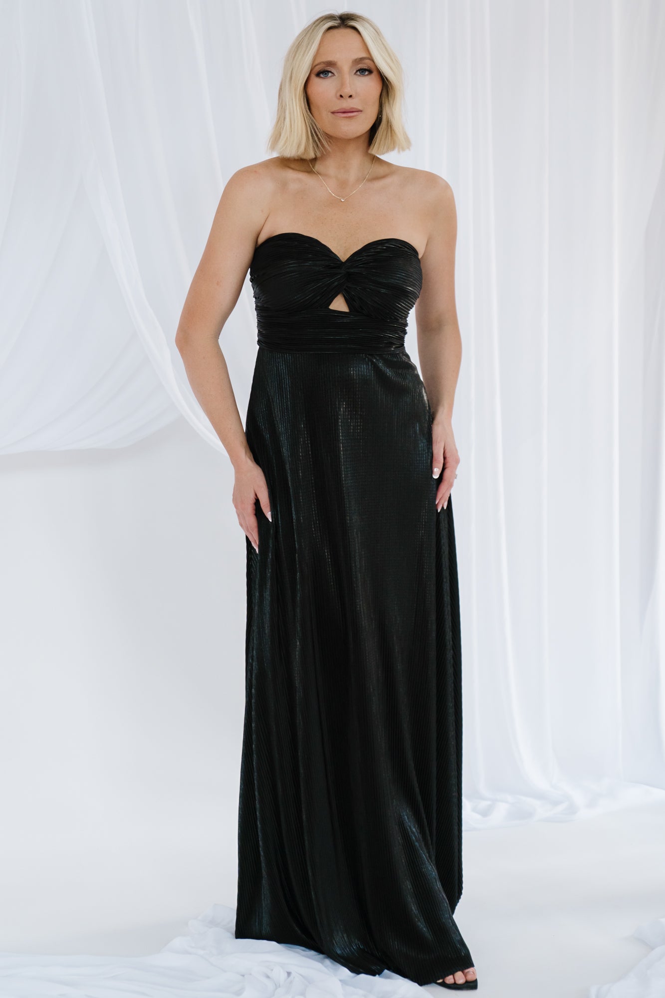 Model in full-length Seraphine strapless metallic pleated maxi gown in black, showing flowing skirt and evening silhouette.