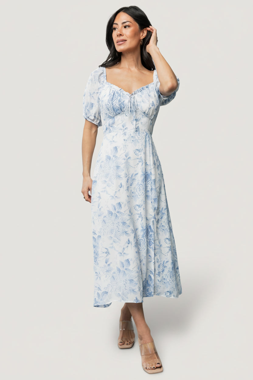 Front view of Cadence Midi Dress in blue floral showing sweetheart peasant neckline, ruffle trim, faux tie, puff sleeves, and A-line midi silhouette.
