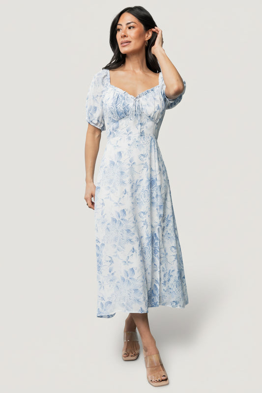 Front view of Cadence Midi Dress in blue floral showing sweetheart peasant neckline, ruffle trim, faux tie, puff sleeves, and A-line midi silhouette.