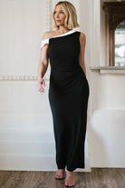 Front view of Valena asymmetrical maxi dress in black with ivory neckline trim, gathered off-shoulder sleeve, fitted waist and flowing skirt.