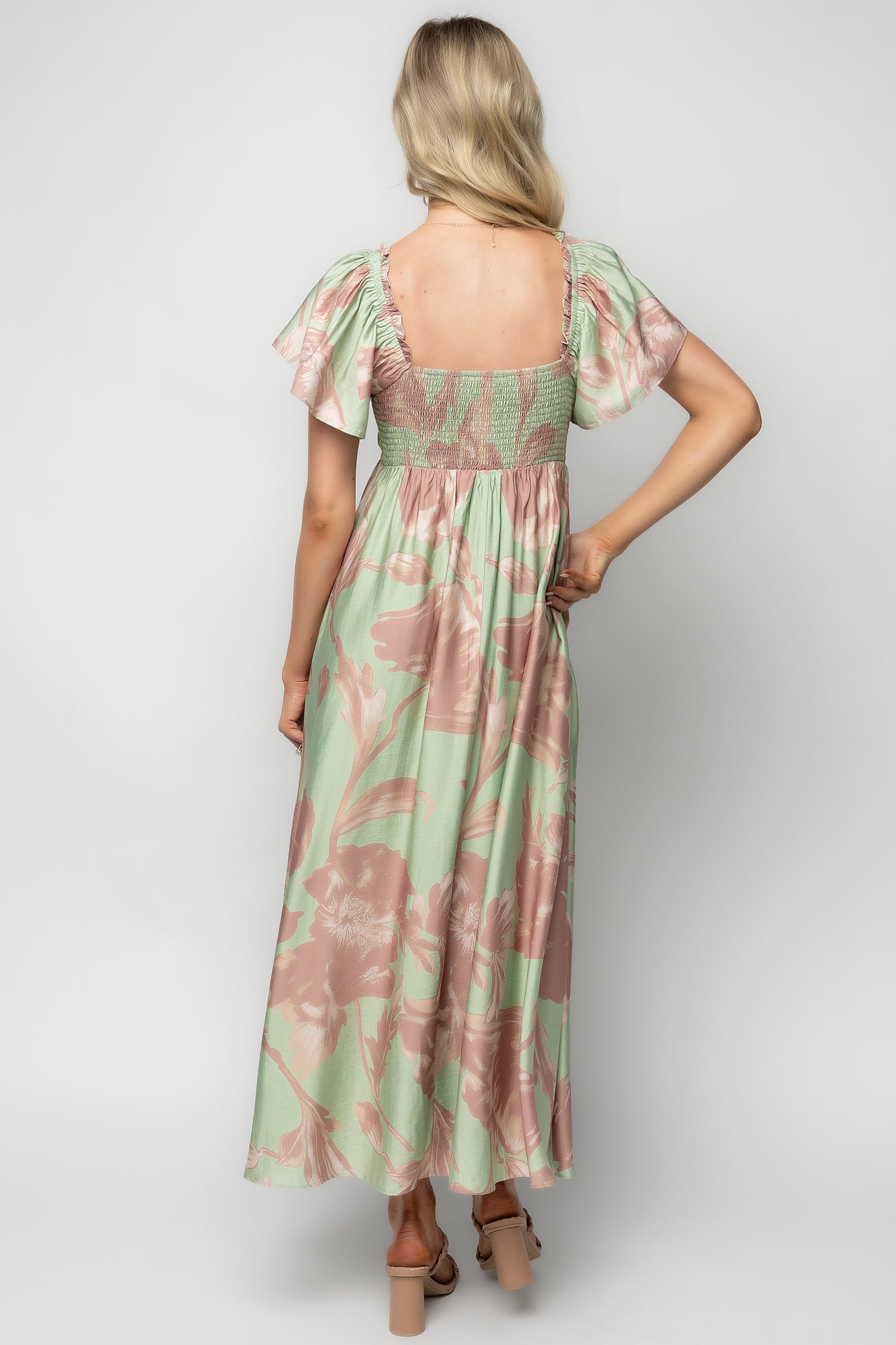Back view of the Eliana Maxi Dress showing the smocked back panel, gentle gathers at the waist, and the sage background with rose-pink floral pattern.