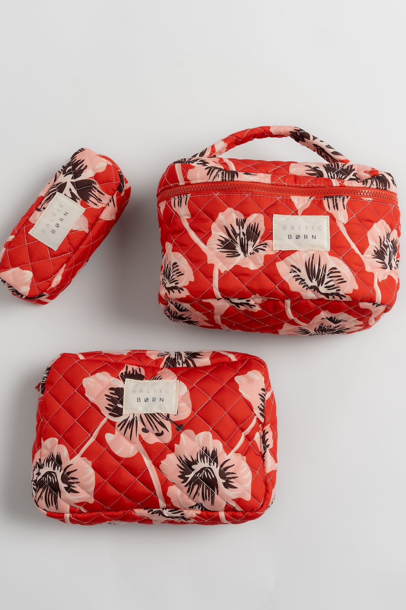 Two red floral-patterned cosmetic bags on a light gray background