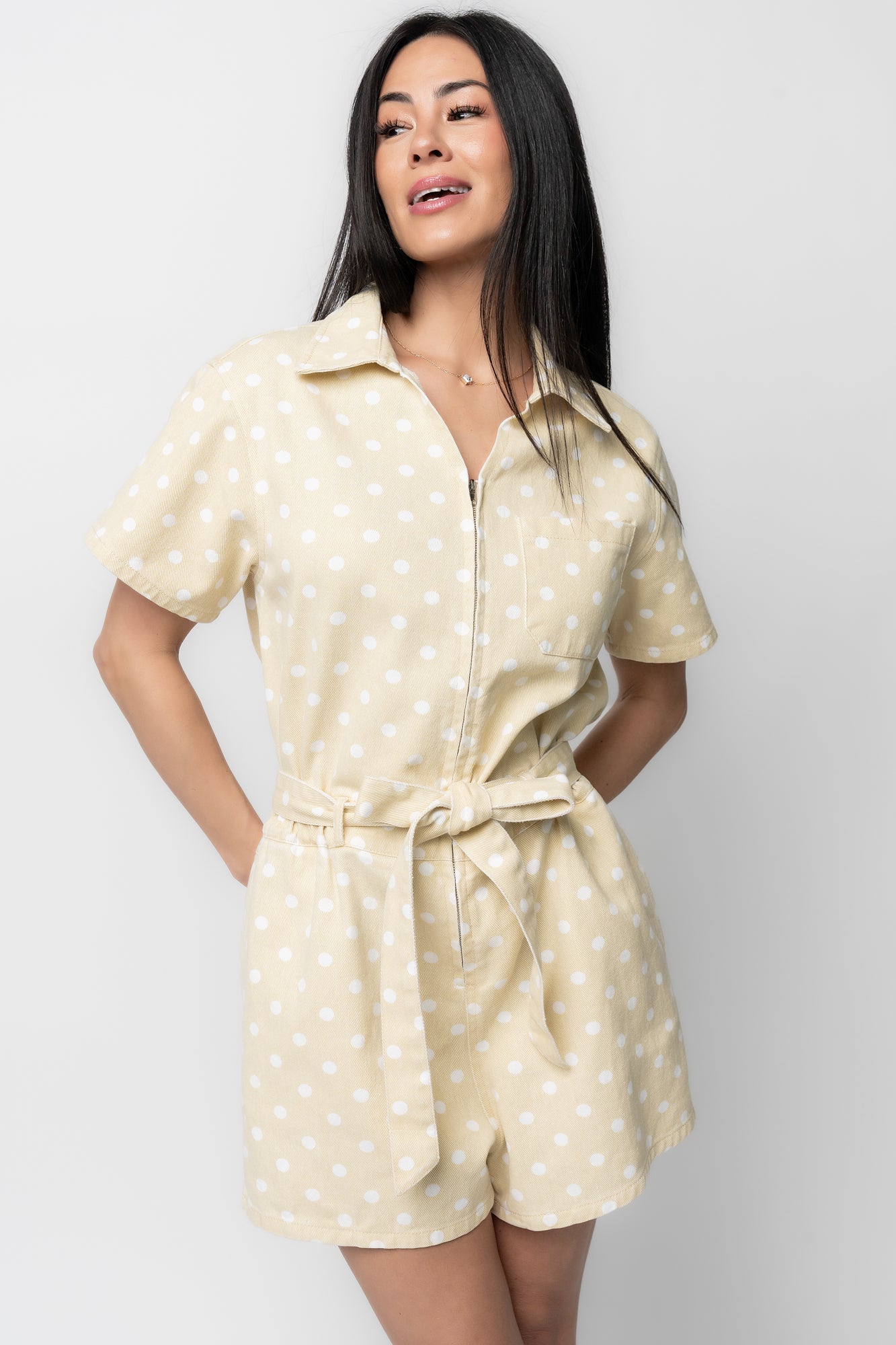 Detail shot of front chest pocket, zipper hardware, and collar construction on the light yellow polka-dot romper.