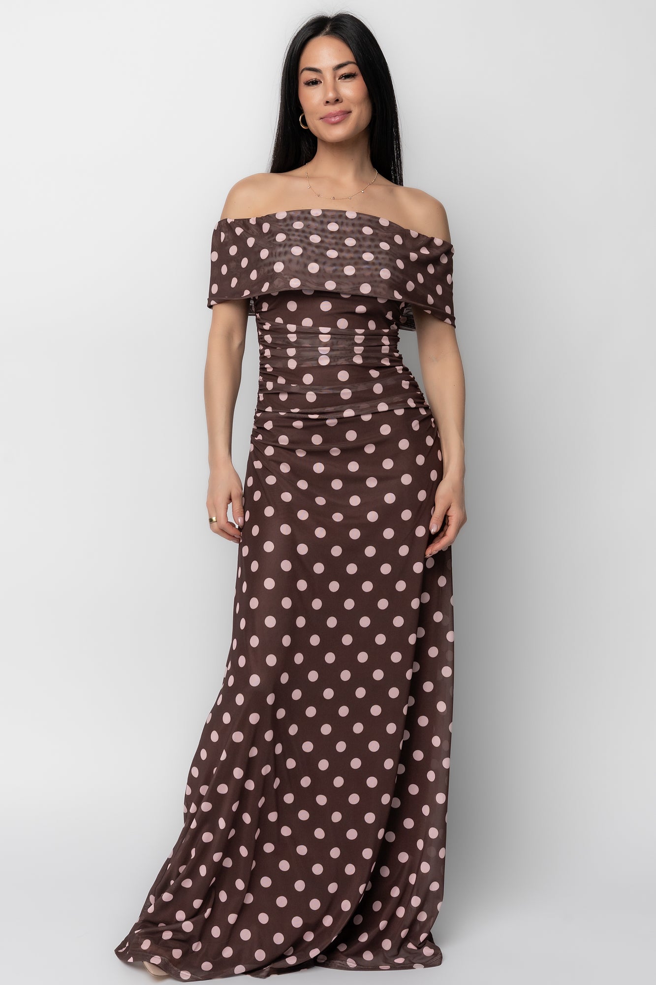 Front view of model wearing Maisie off-shoulder maxi dress in chocolate with blush polka dots, showing fitted bodice and skirt.