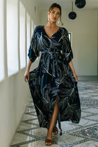 Model wearing Kalea navy maxi dress with off-white botanical print, surplice neckline and detached sash, full-length front view on studio background.