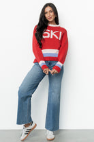 Model wearing the red multi Gilli ski sweater styled with jeans; shows relaxed silhouette, drop shoulder sleeves, and playful color accents.