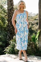 Model styling the Brisa one-shoulder dress with hands in hidden pockets, illustrating practical design and relaxed silhouette in floral print.