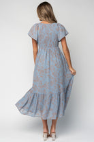 Back and movement shot of the dusty blue dress showing skirt drape, single bottom tier, and subtle sheen of the fabric.