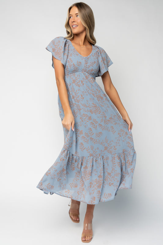 Front view of Monica Smocked Maxi Dress in dusty blue with terracotta floral print, V-neckline and flutter sleeves, full-length view.