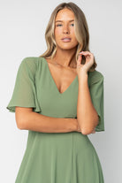 Three-quarter view showing olive Valetta maxi dress drape and left-side leg slit, highlighting movement and chiffon texture.