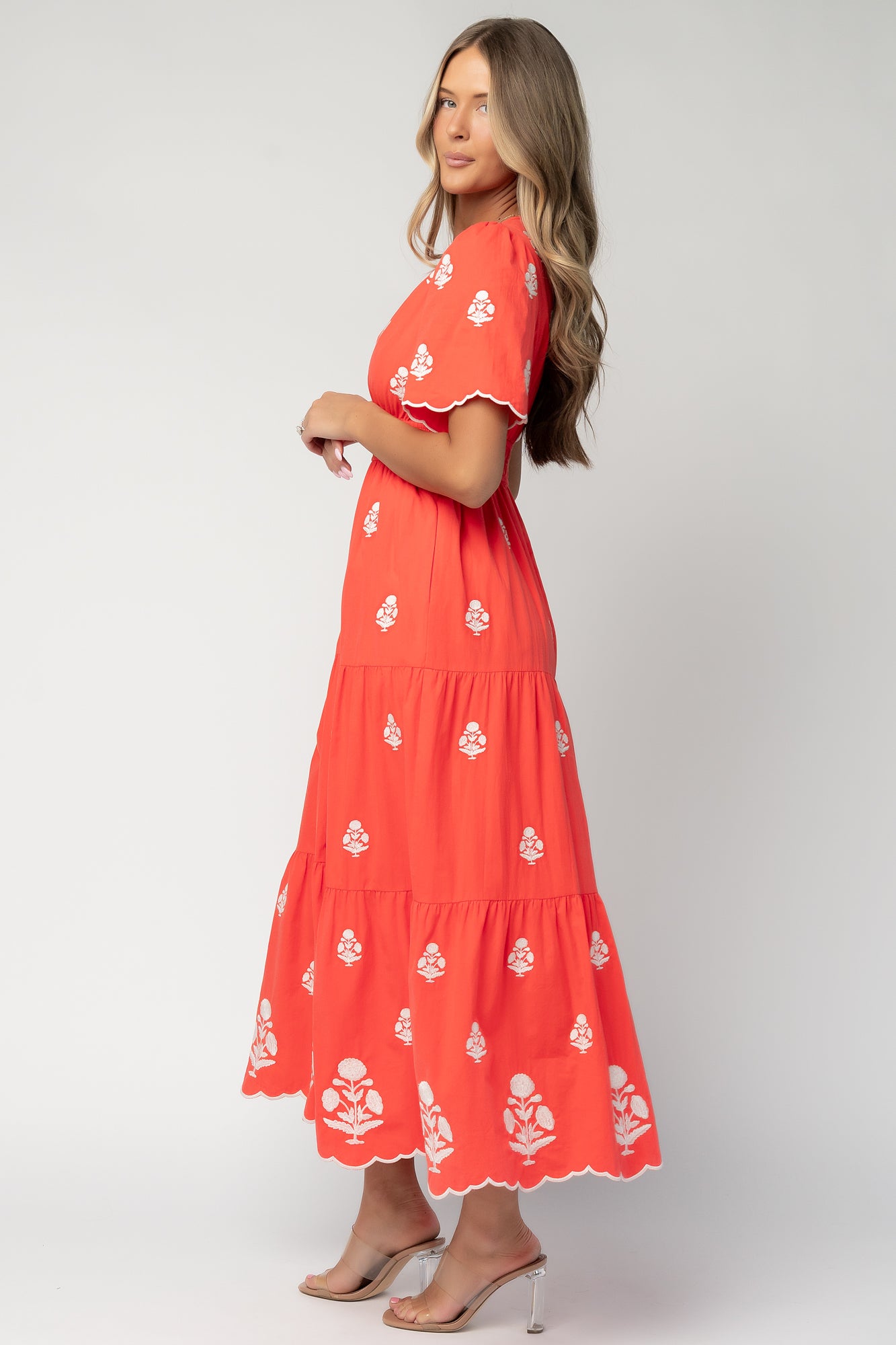 Close-up of off-white floral embroidery on the Delilah dress, highlighting thread detail and scalloped sleeve hem on tomato-red cotton.