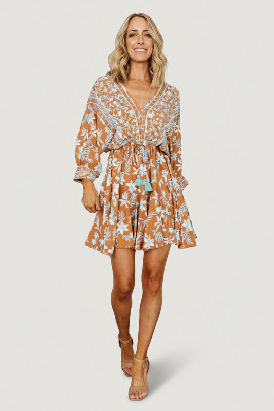 Front view of Adria Mini Dress in camel and blue floral print, deep V-neck, adjustable tassel waist and ruffle hem, on model.