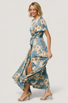 Side view of Agnes satin maxi showing natural waist tie, left leg slit and graceful skirt sweep in teal and gold.