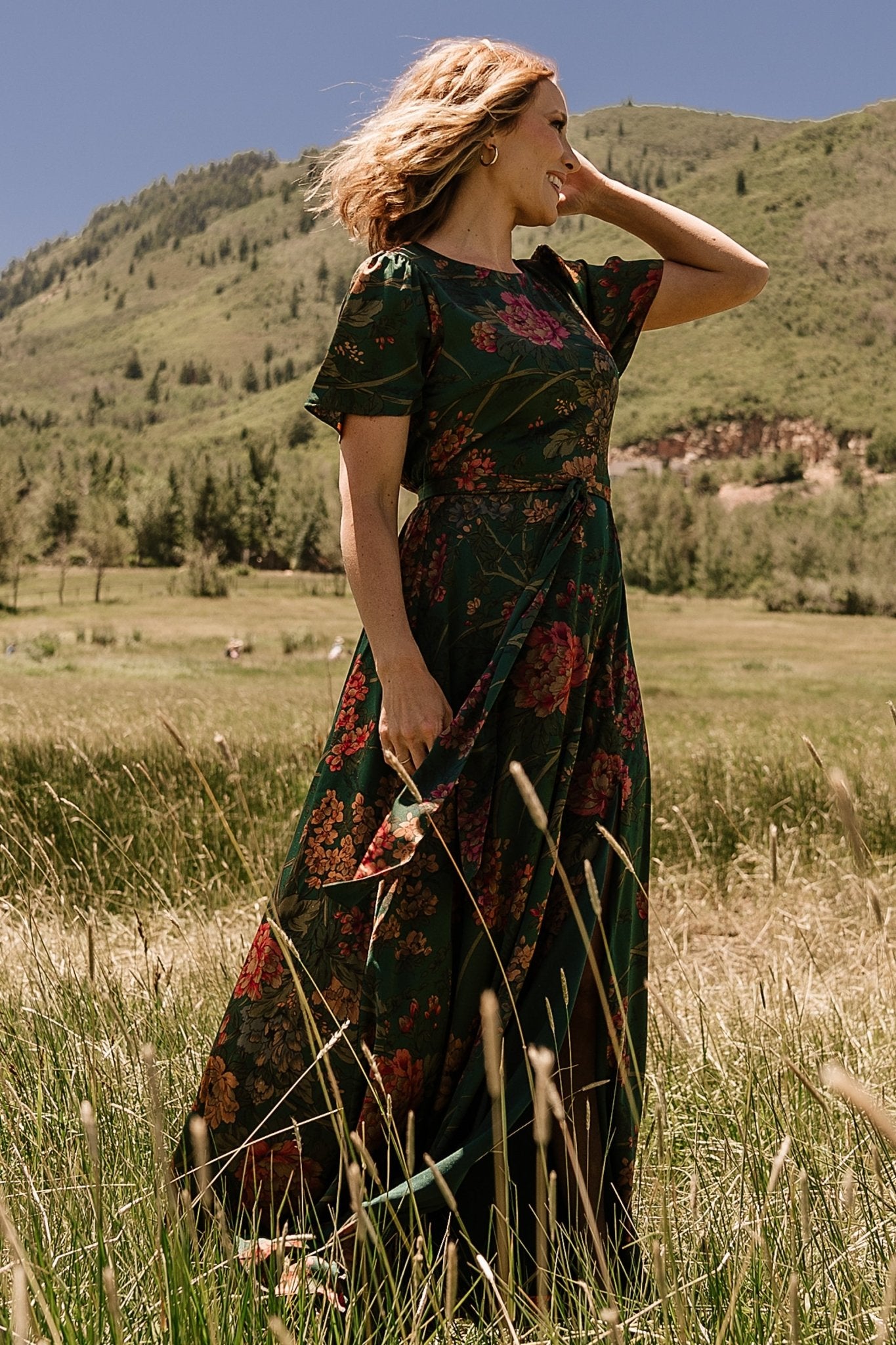 Close fabric texture and seam details of the dark green floral satin maxi dress showing lining edge and hem finish.