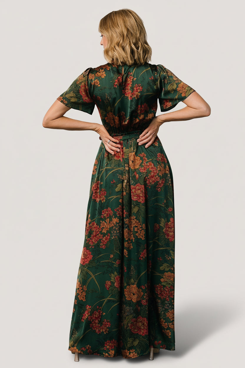 Model in motion wearing dark green floral satin maxi dress to show skirt movement, soft drape, and left leg slit effect.