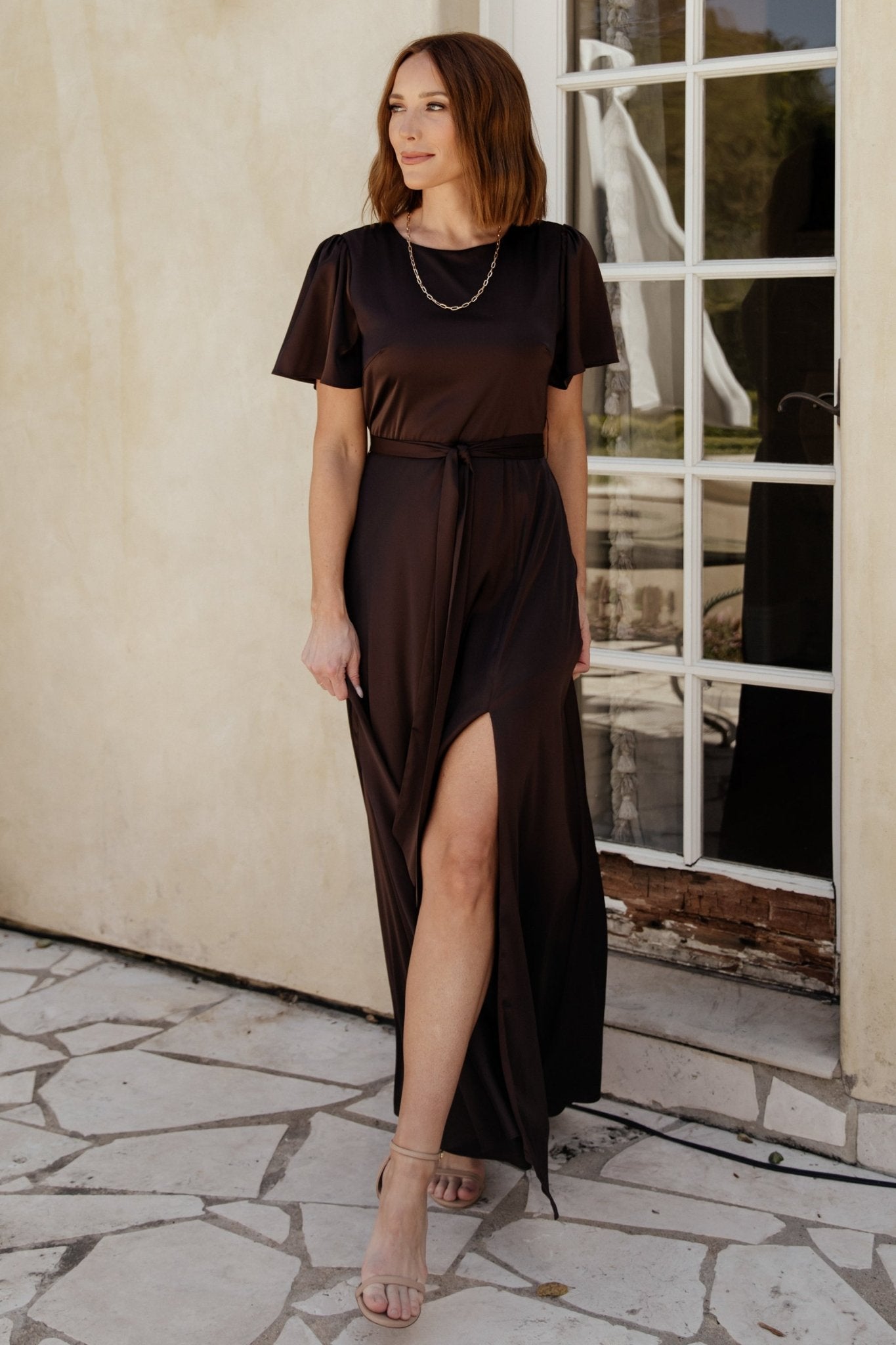 Alternate angle of the Agnes satin maxi in espresso illustrating the dress’ silhouette, short flutter sleeves, and left leg slit detail.