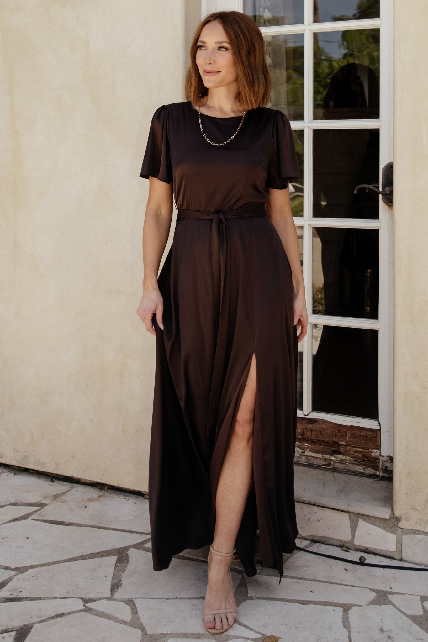 Full-length model image of the Agnes espresso satin maxi, highlighting skirt sweep and left leg slit for elegant movement.