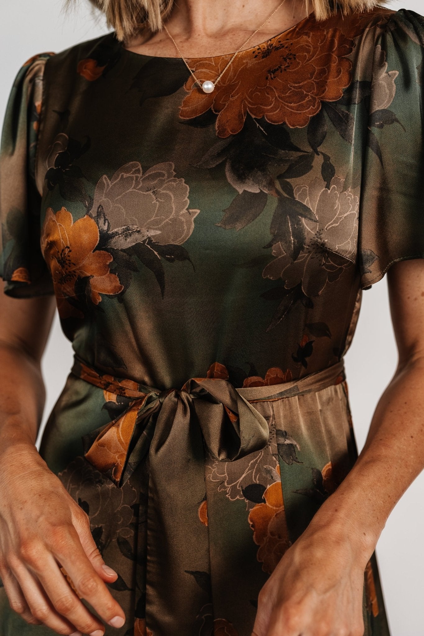 Close-up of flutter sleeve and neckline of olive floral satin dress revealing construction and unlined sleeve detail.
