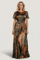 Front full-length view of olive floral satin maxi dress with rounded neckline, flutter sleeves, removable sash, and flowing skirt.