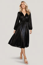 Model wearing Aisha Shimmer Midi Dress in black standing full-length to display overall silhouette, midi hem, and shimmer fabric.