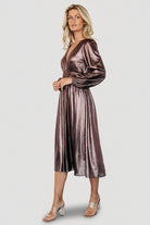 Front view of bronze Aisha shimmer midi dress on model showing deep V-neck, smocked waist, and gathered flowing skirt.