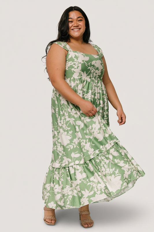 Green and ivory floral maxi dress worn by model, square neckline, smocked back, gathered tank cap sleeves, and functional side pockets on display.