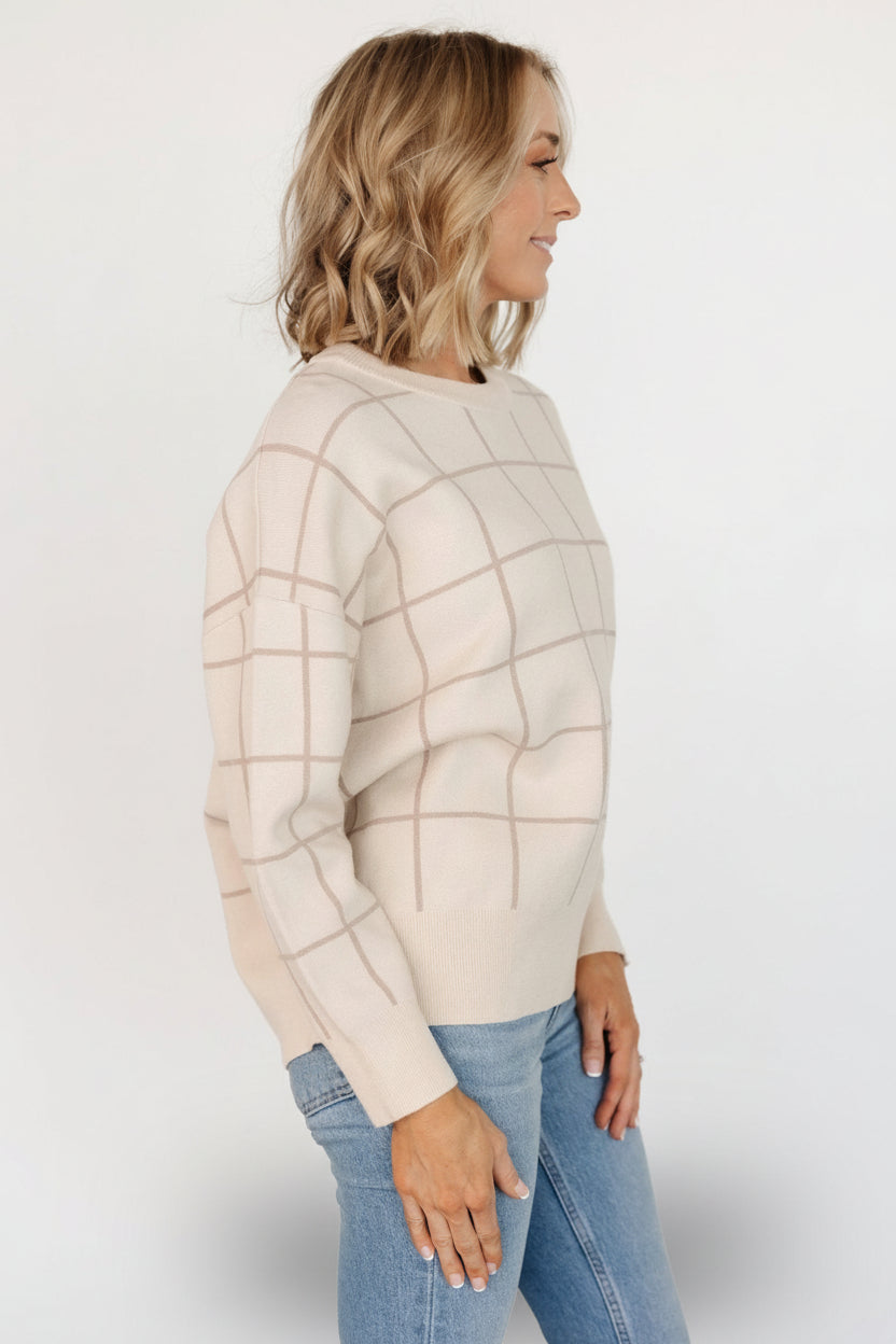 Close-up of knit fabric showing oatmeal base and taupe windowpane stitch detail, plus textured ribbing at hem and cuff.