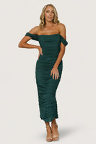 Front view of peacock mesh midi dress on model, fitted bodycon silhouette with ruched side seams and structured bust detail, midi hem and back slit visible in profile, styling with minimal jewelry and heels.