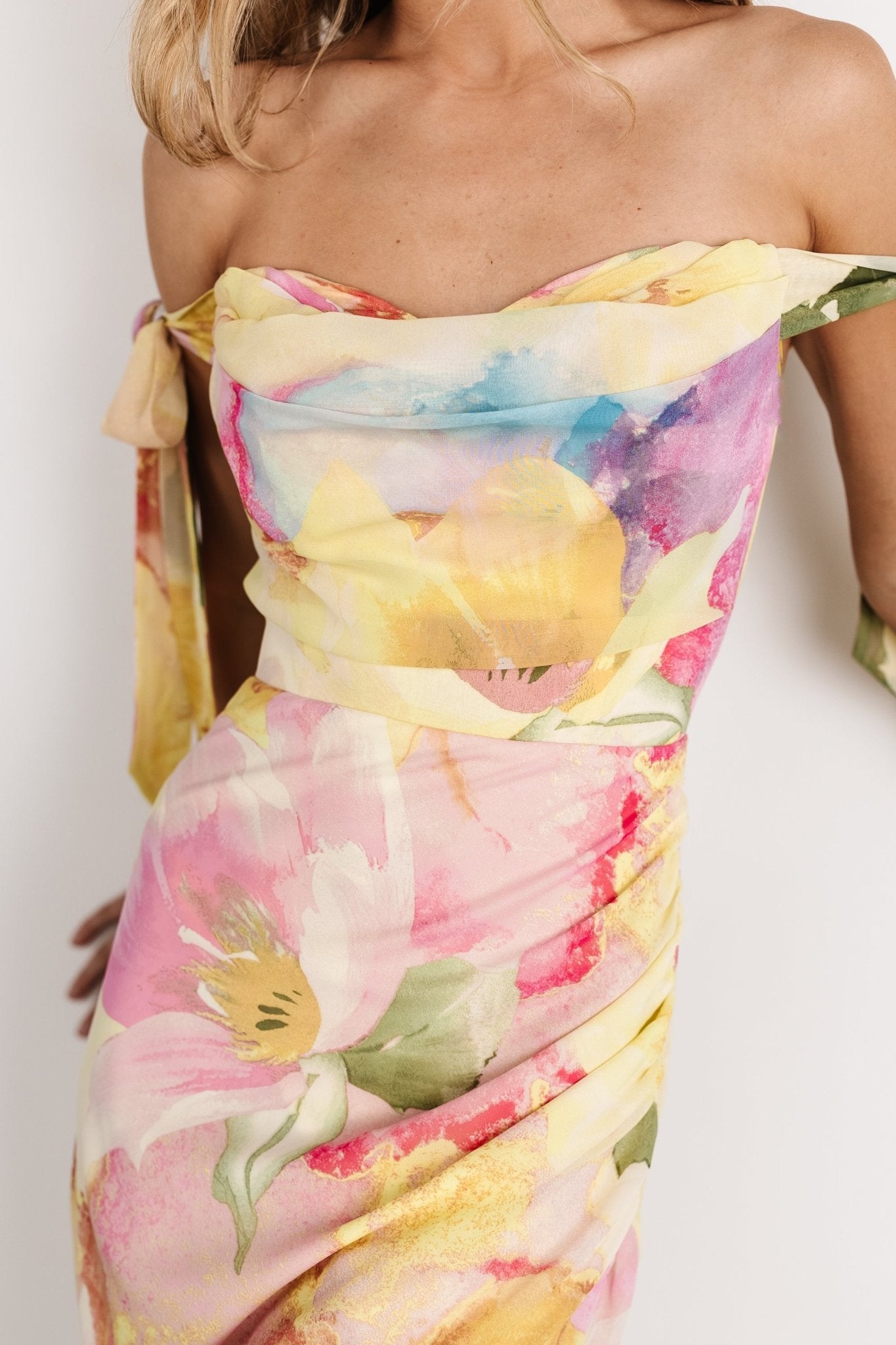 Three-quarter model view of the multi-floral chiffon maxi dress highlighting flowing tulip skirt, off-shoulder bow straps, and pastel floral print.