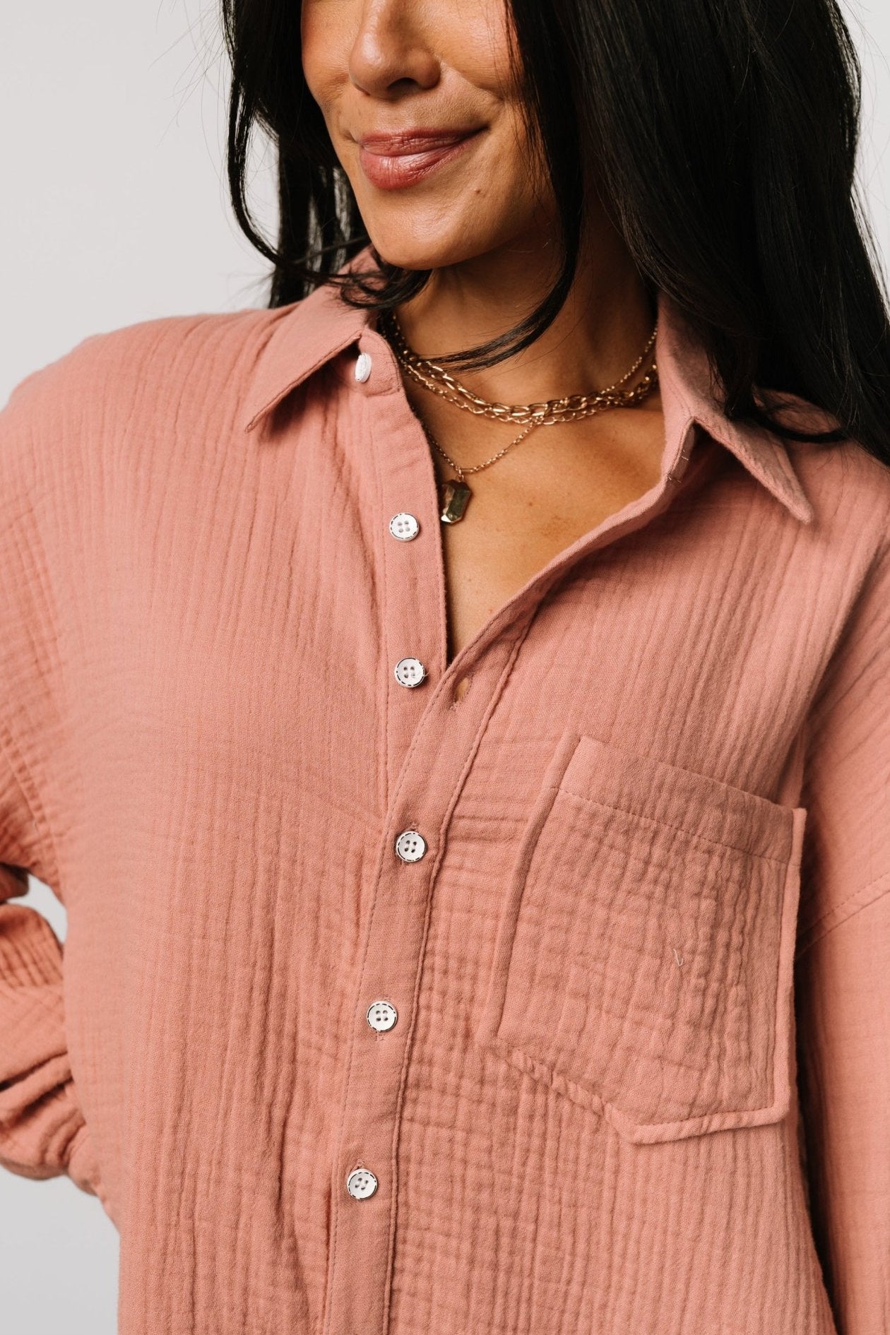 Three-quarter view of the dusty rose shirt dress highlighting the asymmetrical hemline, long sleeves with buttoned cuffs, and relaxed oversized fit.