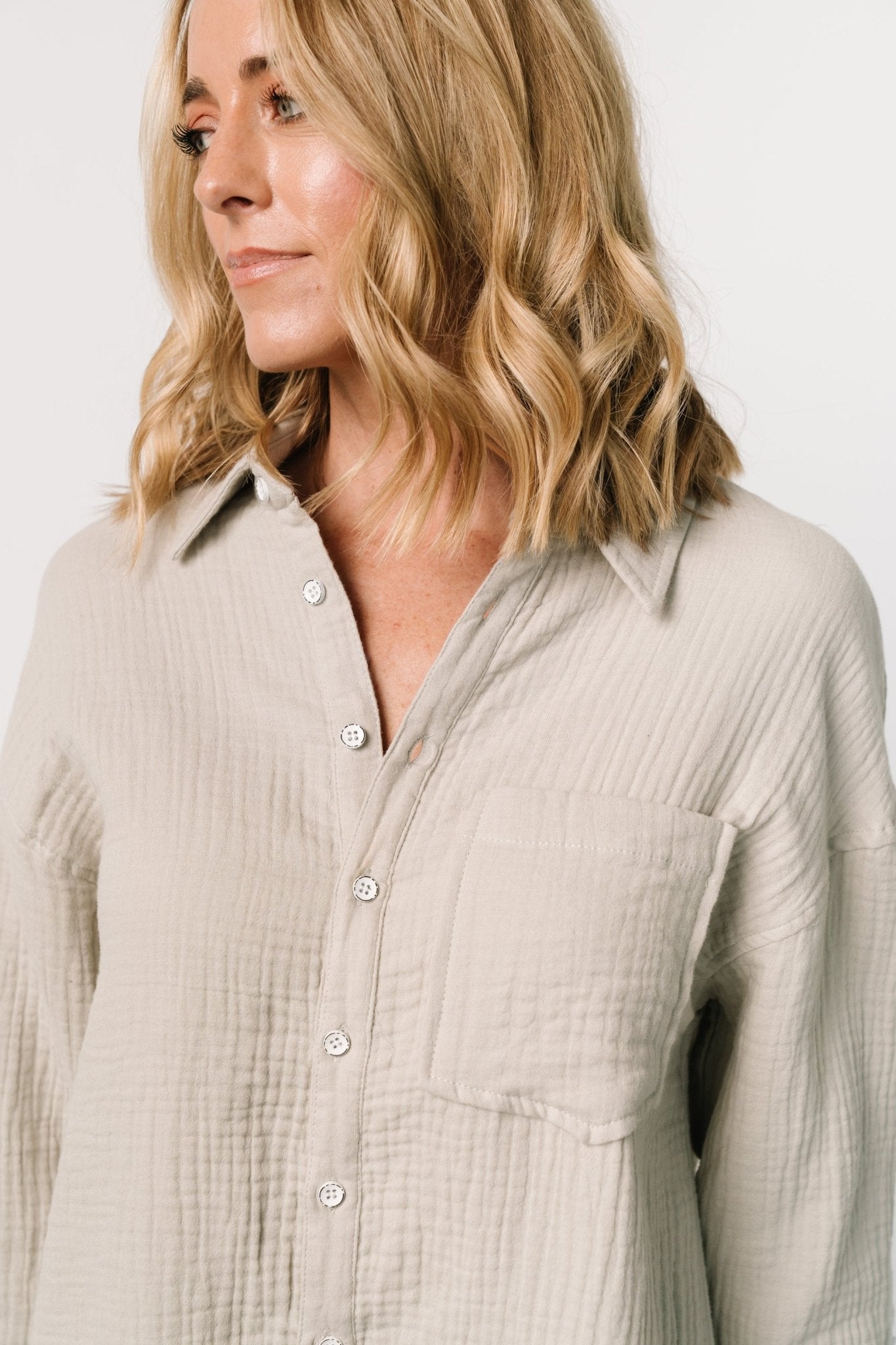 Detail close-up of button-front, cuff buttons, and collar on the light sage oversized shirt dress showing fabric texture and finish.