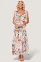 Front view of blush multi floral chiffon maxi dress with square neckline, paneled bodice and three ruffled tiers, fully lined.