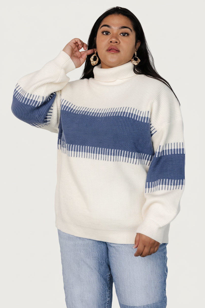 Model wearing the Antonov sweater in blue and cream, styled with jeans to show drape, length, and ribbed trim at neckline and hem for proportion.