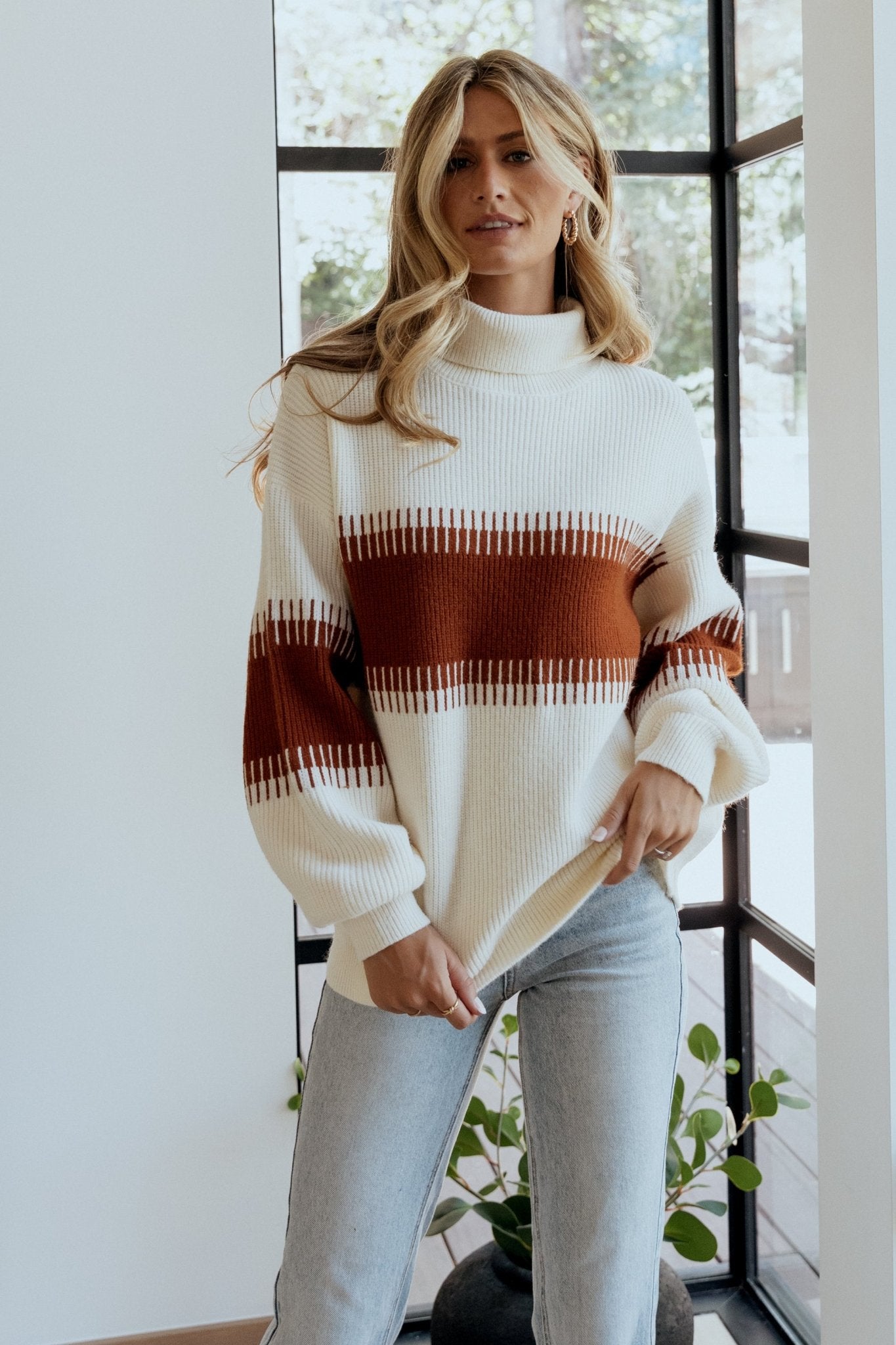 Full-length shot of cream and spice Antonov sweater styled with jeans, showcasing relaxed silhouette, turtle neckline, and contrast colorblock panels.