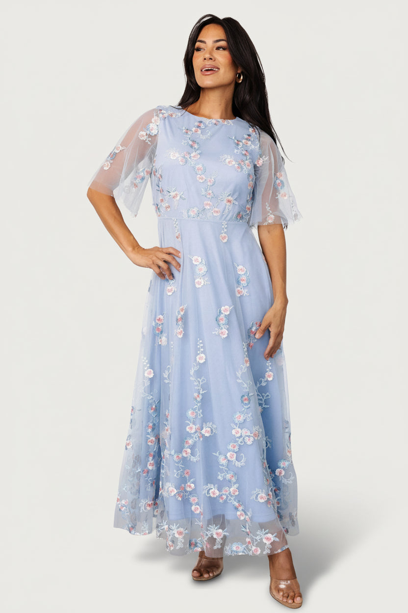Front view of Arabella light blue tulle maxi dress with blush embroidered floral motifs, round neckline and flowing layered skirt.