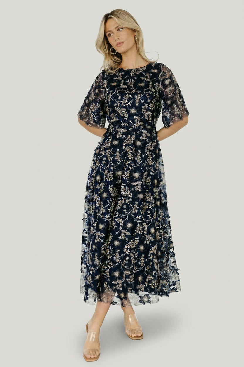 Styled look of the Arabella navy tulle maxi dress with gold embroidery, showing round neckline, short sleeves and flowing maxi length.
