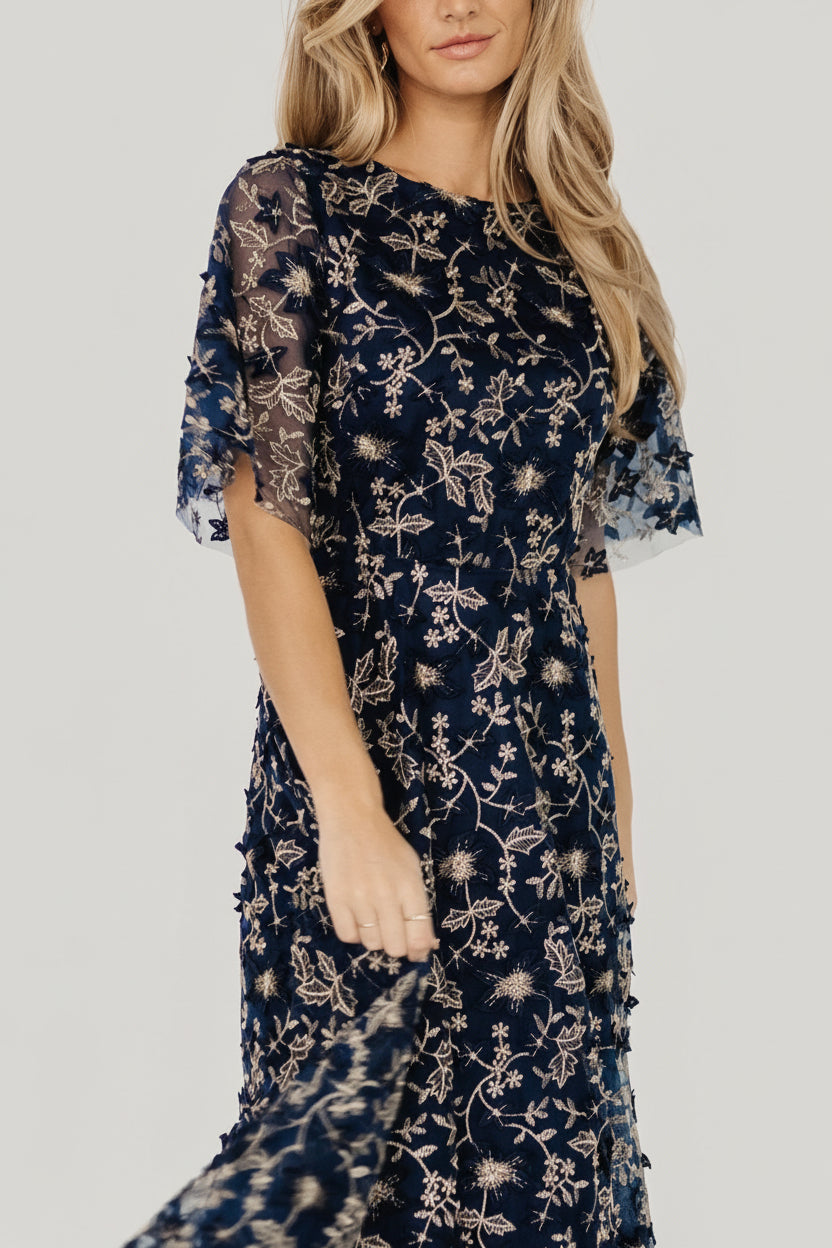 Side view of navy tulle maxi with layered skirt and delicate gold floral embroidery cascading from bodice to hem for an elegant finish.