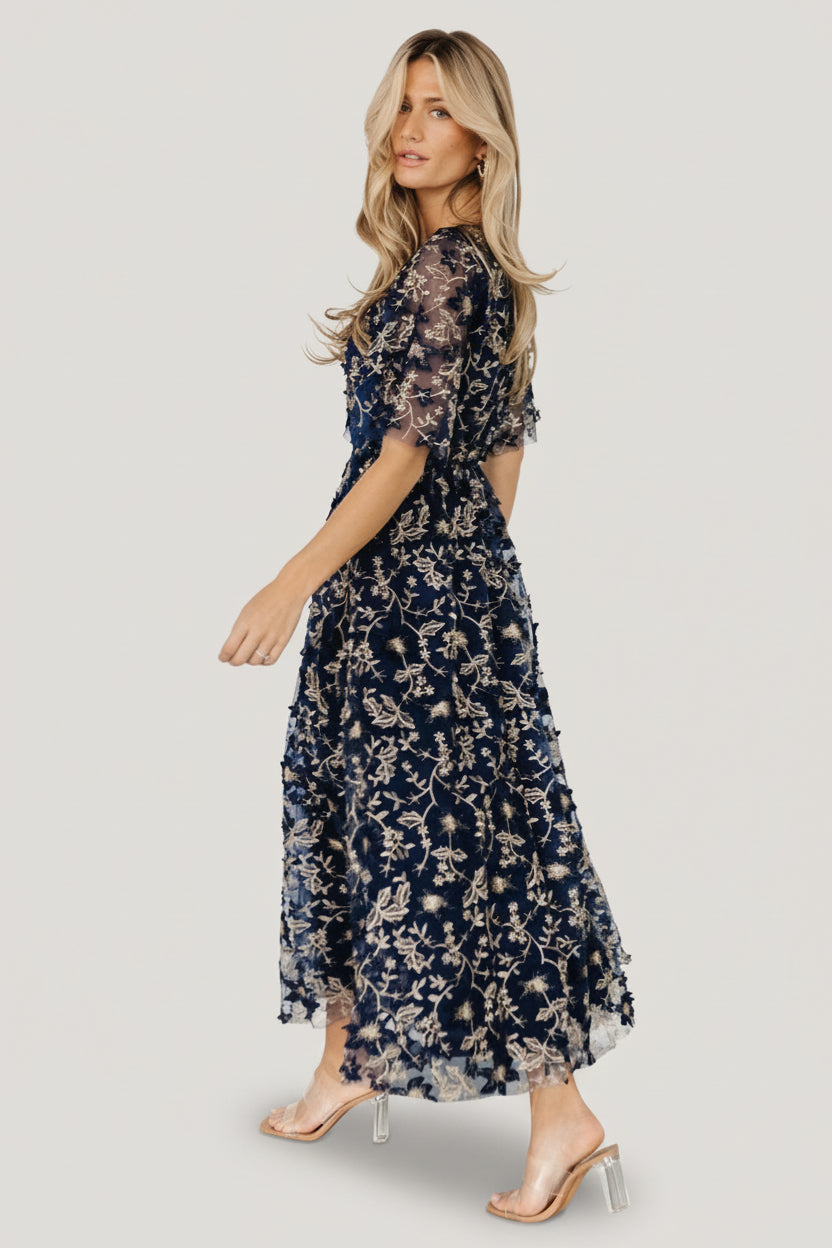 Back view highlighting keyhole button closure and elasticized back waist on navy tulle maxi dress with gold embroidered florals.