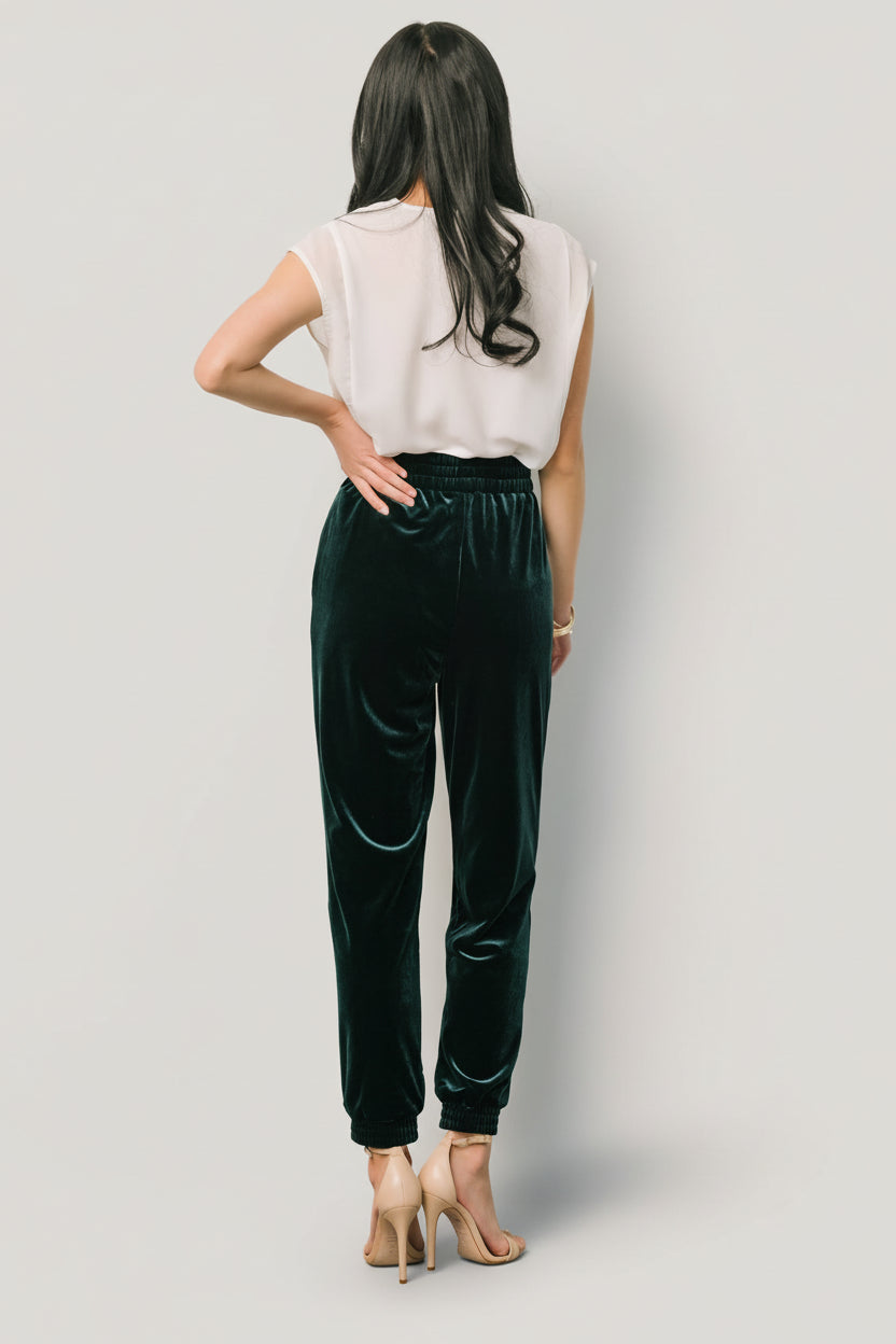 Styled outfit shot with Archie velvet jogger pants in dark green paired with a knit top, illustrating versatility for day or evening wear.