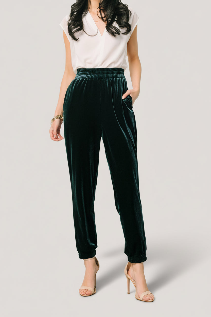 Product flat-lay of Archie velvet jogger pants in dark green highlighting overall cut, elastic ankle cuffs, and pocket placement.