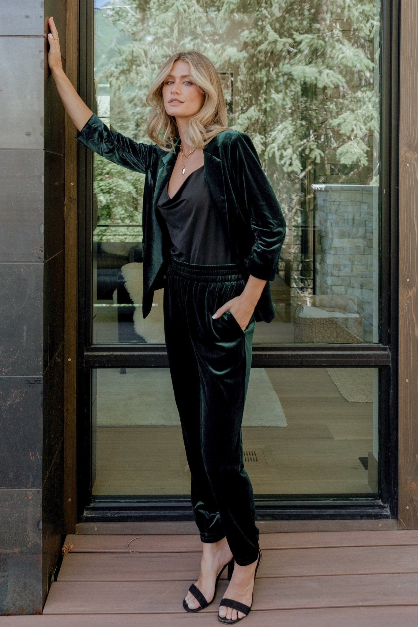 Full-length on-model shot of Archie velvet jogger pants in dark green with hands-in-pockets styling and visible fabric drape and sheen.