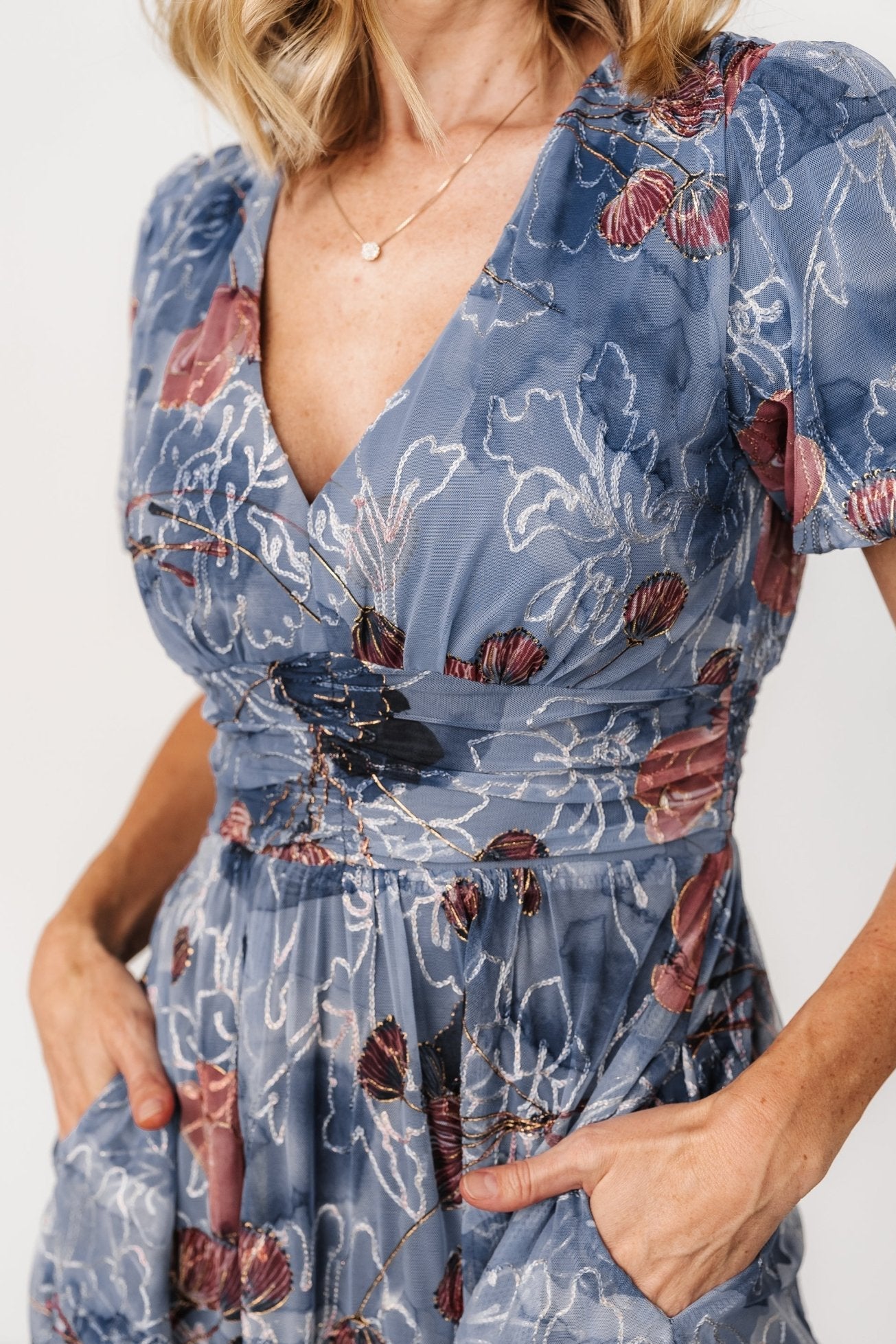 Close-up of embroidered floral tulle overlay with subtle gold accents and soft mesh beneath, showing texture and delicate stitching on the bodice.