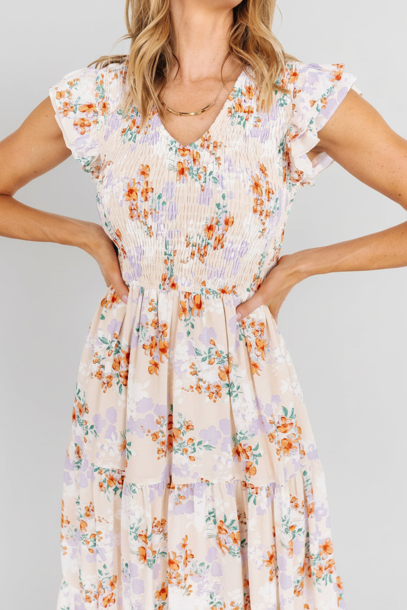 Detail shot of ruffle sleeve layers and floral print on cream chiffon smocked maxi dress, showing print colors and texture.