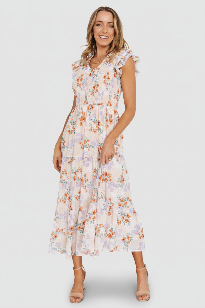 Cream floral chiffon maxi dress with smocked bodice, V-neck, ruffle short sleeves and tiered skirt, front model view, pockets visible.