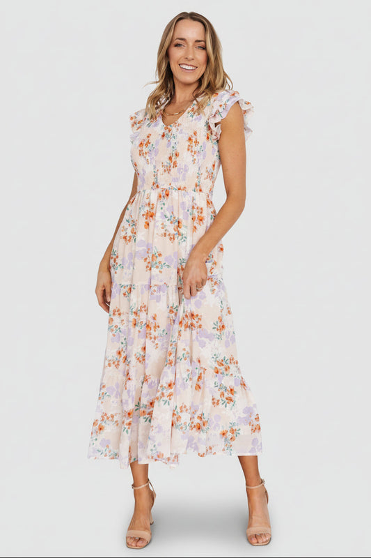Cream floral chiffon maxi dress with smocked bodice, V-neck, ruffle short sleeves and tiered skirt, front model view, pockets visible.