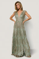 Three-quarter view showing the high banded waist and flowing maxi skirt of the Arlene Shimmer Gown in sage and gold, with subtle metallic shimmer.