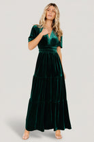 Back and side angle of emerald Artemis velvet maxi, showing tiered skirt flow, elastic waist detail, and full-length hemline.