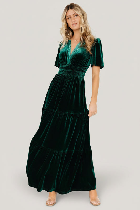 Front view of emerald Artemis velvet maxi dress with plunging V-neck, short flutter sleeves, elastic gathered waist, and tiered skirt.