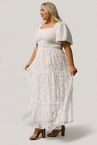 Studio detail shot of off-white lace maxi focusing on sleeve hem, ruffle trim, and textured lace overlay fabric.