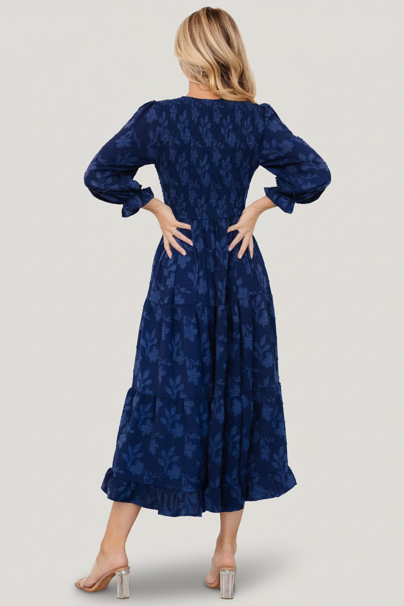 Back view of navy floral tiered midi dress showing smocked back bodice, ruffled sleeve cuffs, and flowing skirt tiers.